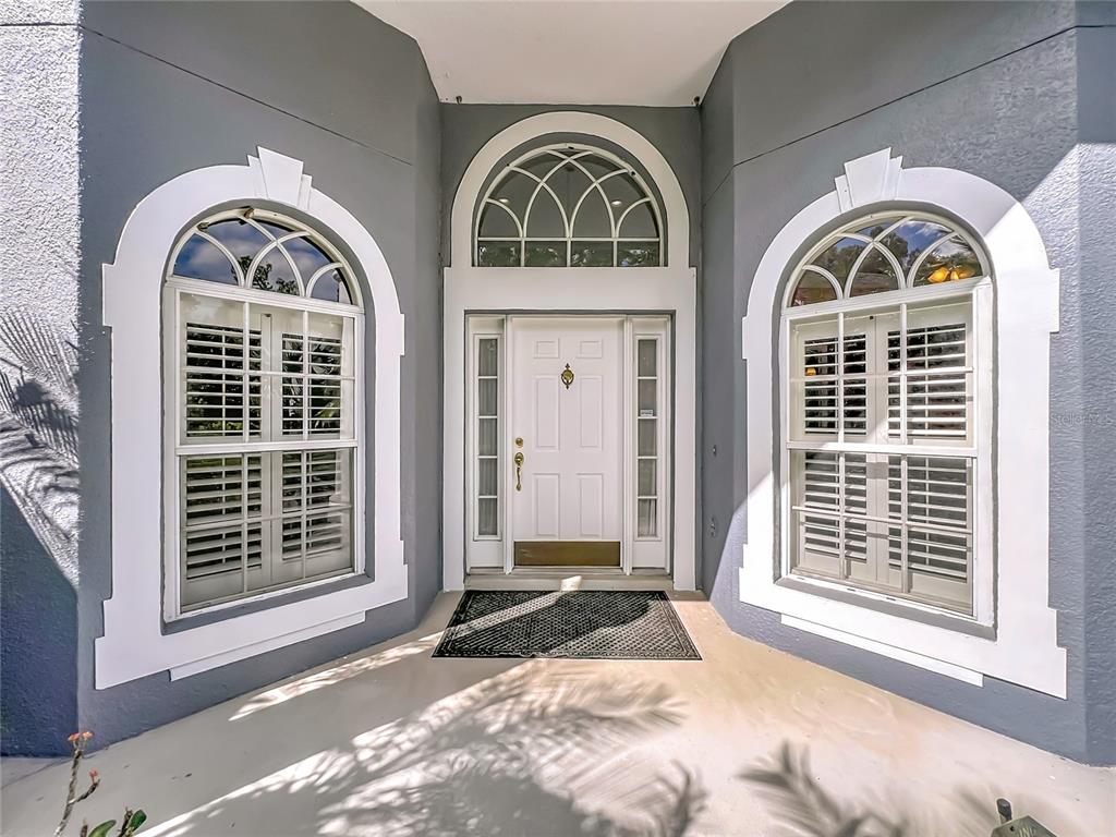A white front door with sidelights and arched windows is centered between two large windows — 809 MUIRFIELD CIRCLE, APOPKA, FL