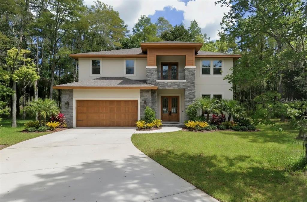 A two-story house with a stone facade, wood garage door, and a second-story balcony — 19832 WESTWOOD LANE, LAND O LAKES, FL