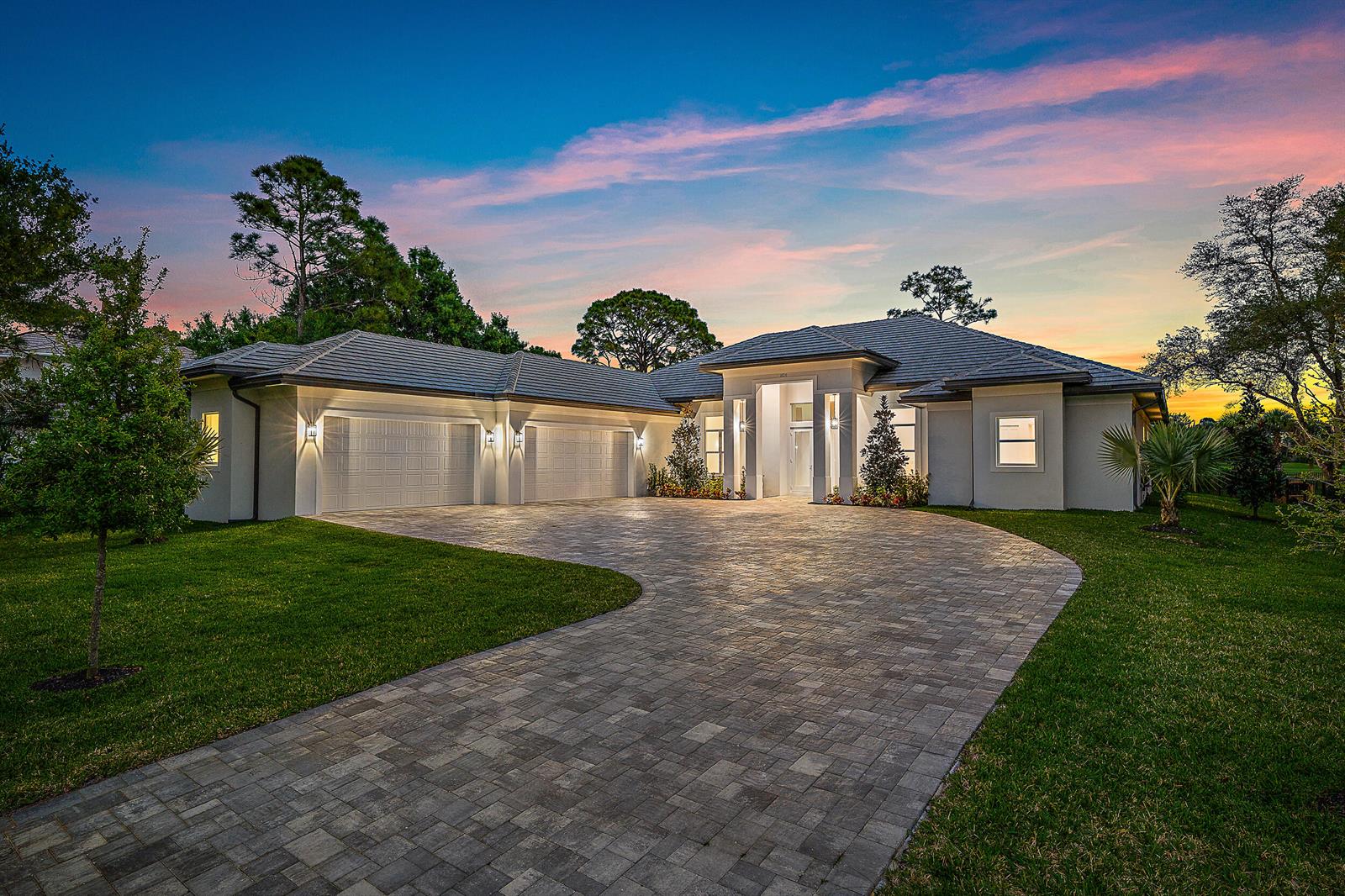 A modern single-story house with a three-car garage and a paved driveway at sunset — 18211 SE Old Trail Drive W, Jupiter FL 33478, JUPITER, FL