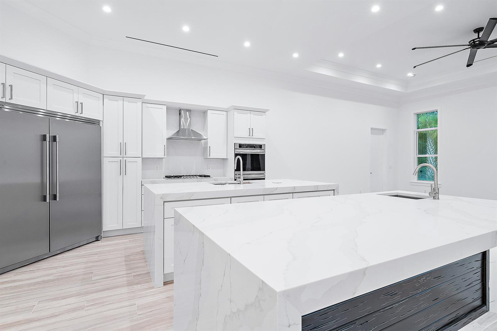 A modern kitchen features white cabinetry, stainless steel appliances, and two large marble-topped islands — 18211 SE Old Trail Drive W, Jupiter FL 33478, JUPITER, FL