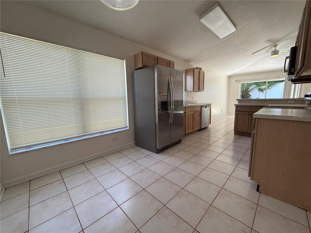 A kitchen features light-colored tile flooring, stainless steel appliances, and wood cabinetry — 1905 PINE BAY DRIVE, LAKE MARY, FL