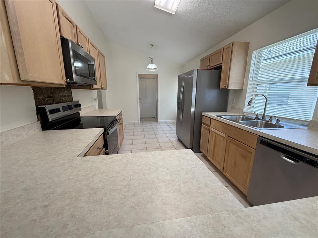 A kitchen features light wood cabinets, stainless steel appliances, and light-colored laminate countertops — 1905 PINE BAY DRIVE, LAKE MARY, FL