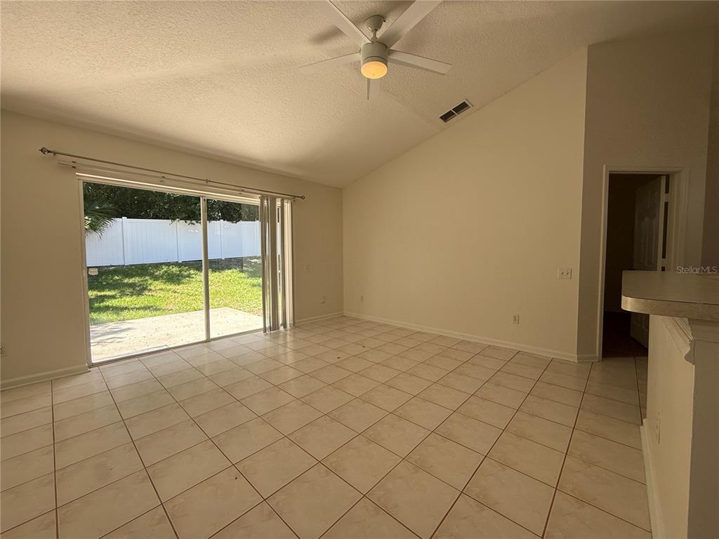 A living room with light tile flooring, a vaulted ceiling, and sliding glass doors to a yard — 1905 PINE BAY DRIVE, LAKE MARY, FL