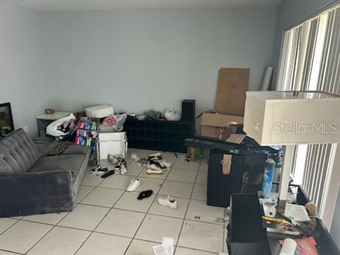 A living room with light-colored tile flooring, a gray sofa, and various items scattered about — 365 S NARANJA AVENUE, PORT ST LUCIE, FL