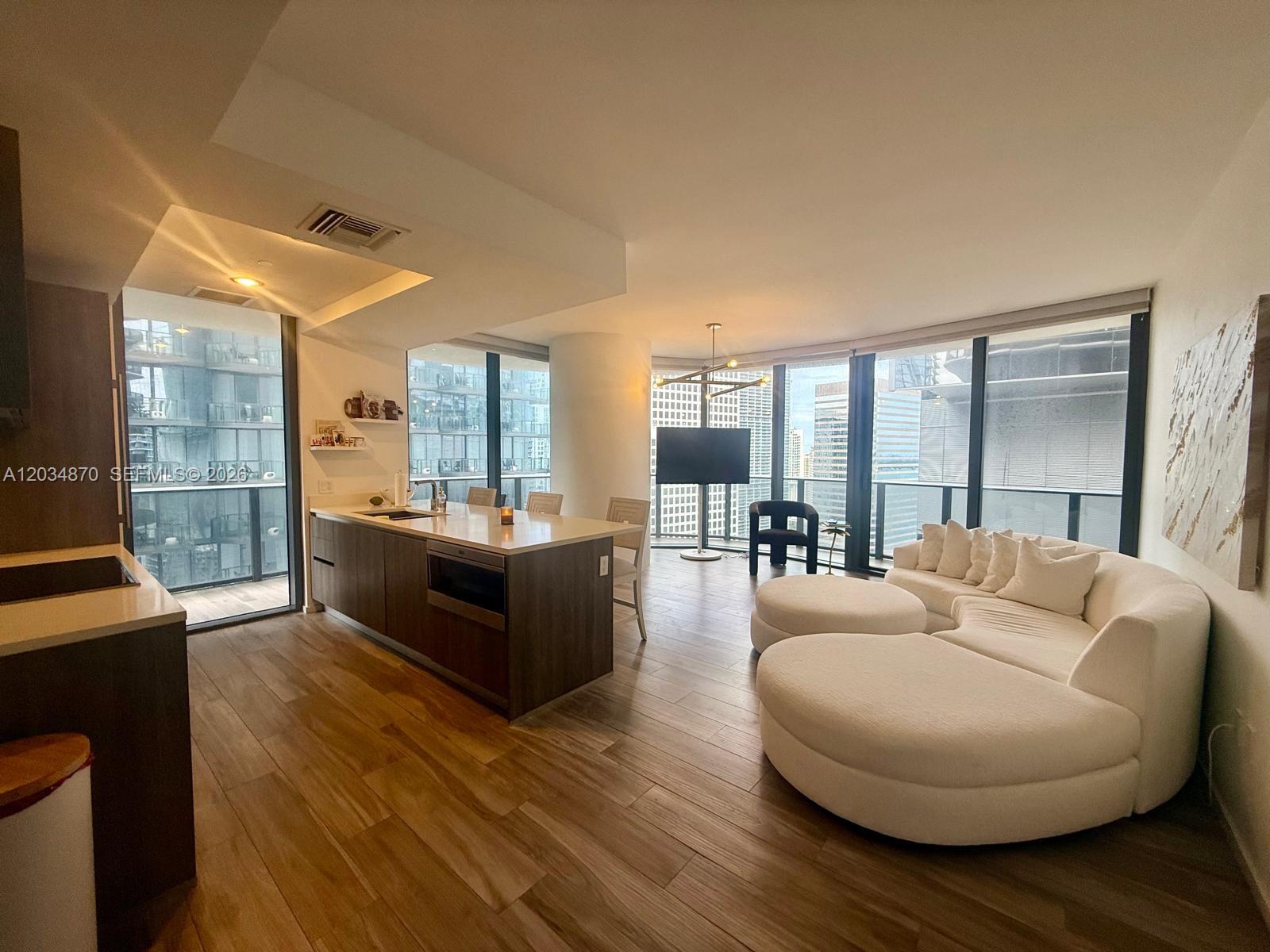 A modern open-concept living area features a kitchen island, white curved sofa, and floor-to-ceiling windows — 801 S Miami Ave # 3005, Miami FL 33130, MIAMI, FL