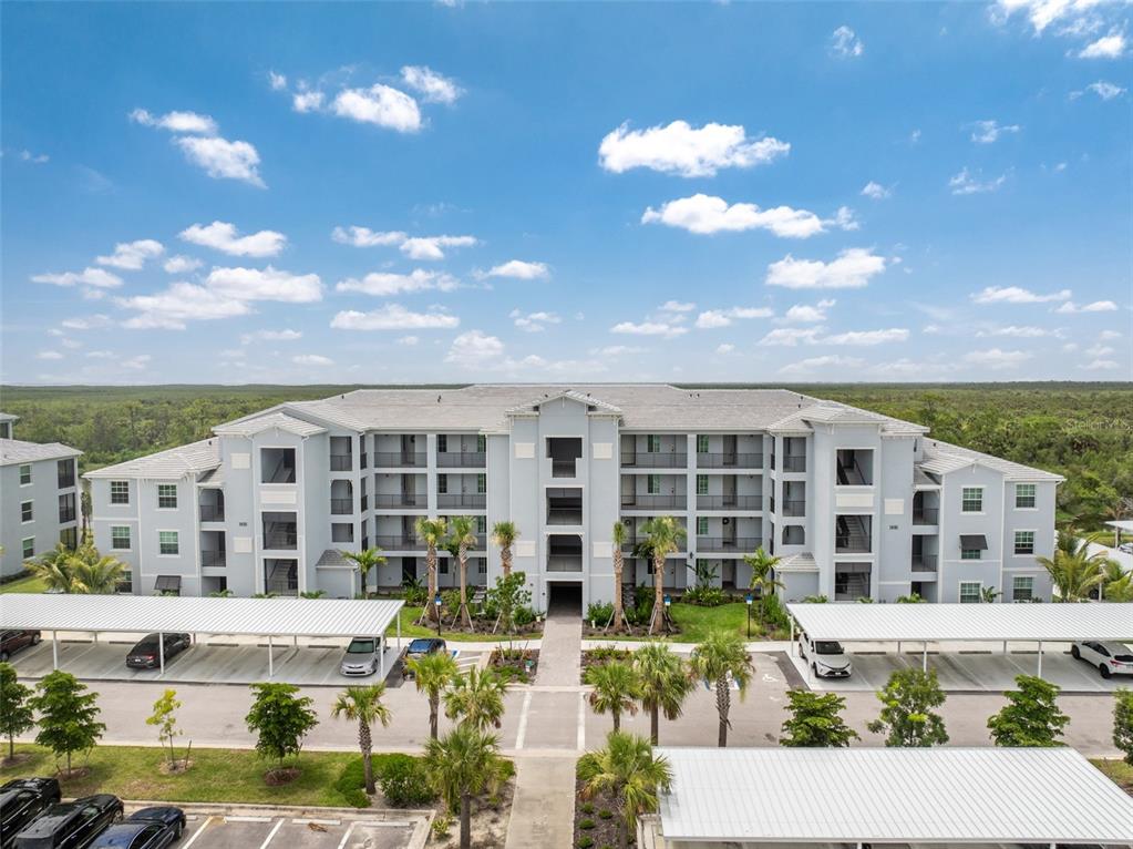 An exterior view of a multi-story apartment building with covered parking and palm trees — 14141 HERITAGE LANDING BOULEVARD UNIT 935, PUNTA GORDA, FL