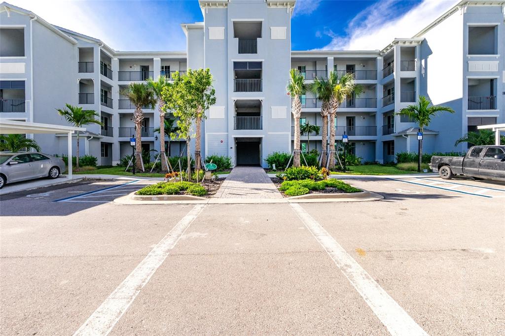 A multi-story apartment building exterior features a central entrance, palm trees, and parking spaces — 14141 HERITAGE LANDING BOULEVARD UNIT 935, PUNTA GORDA, FL