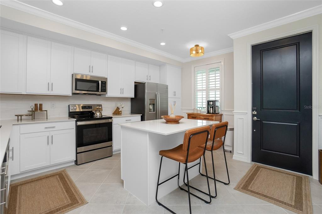 A modern kitchen features white cabinetry, stainless steel appliances, a central island, and a black door — 14141 HERITAGE LANDING BOULEVARD UNIT 935, PUNTA GORDA, FL