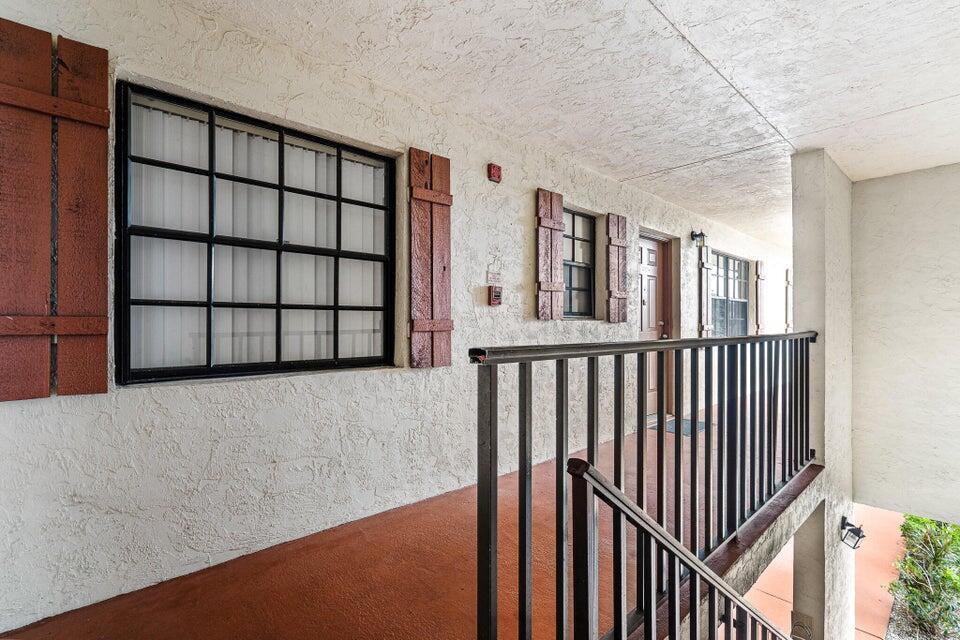 An exterior walkway features a textured stucco wall, dark metal railings, and windows with shutters — 4151 Oak Terrace Drive # 4151, FL 33463, FL