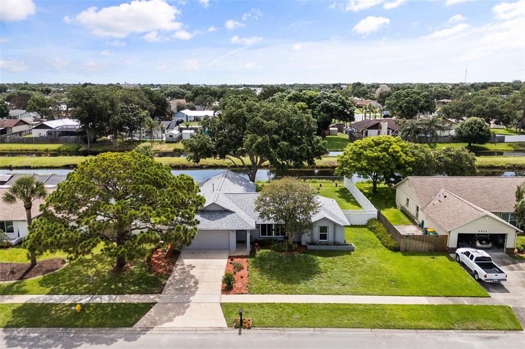 An aerial view shows a single-story house with a gray roof, driveway, and backyard canal — 2427 NOBILITY AVENUE, MELBOURNE, FL