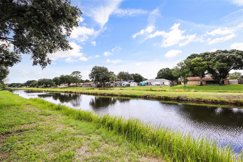 A canal flows past a grassy bank with residential houses and trees in the background — 2427 NOBILITY AVENUE, MELBOURNE, FL
