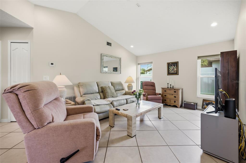 A living room features a vaulted ceiling, tile flooring, a sofa, and several armchairs — 2427 NOBILITY AVENUE, MELBOURNE, FL