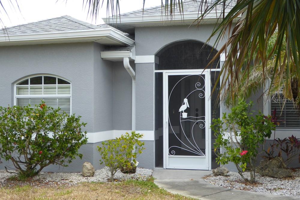 A gray house exterior features a white front door with a decorative pelican screen insert — 328 BAYTREE DRIVE, ROTONDA WEST, FL