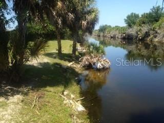 A grassy bank with palm trees borders a calm canal under a clear blue sky — 328 BAYTREE DRIVE, ROTONDA WEST, FL