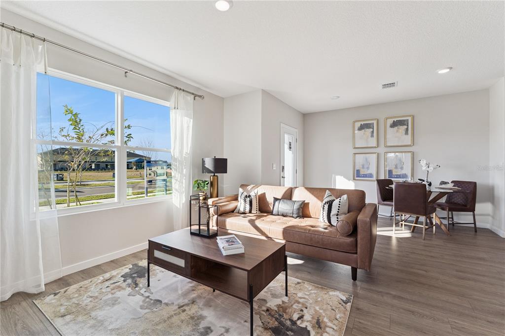 A living room with a brown leather sofa, coffee table, and dining area near windows — 592 PRESTON COVE DRIVE, ST CLOUD, FL