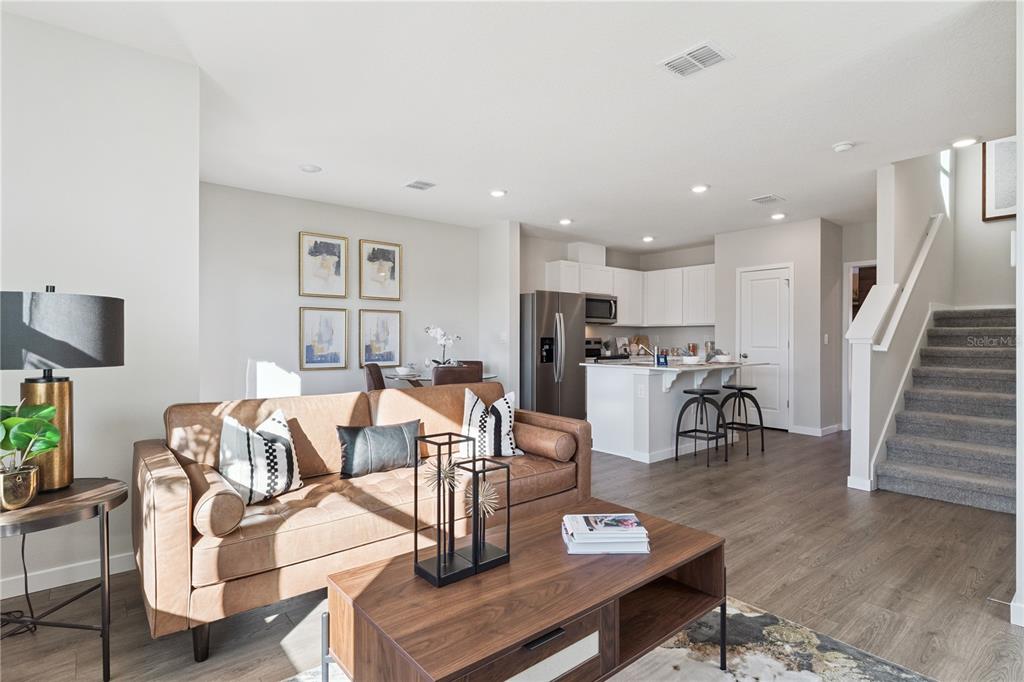 An open-concept living room and kitchen featuring a leather sofa, coffee table, and staircase — 592 PRESTON COVE DRIVE, ST CLOUD, FL