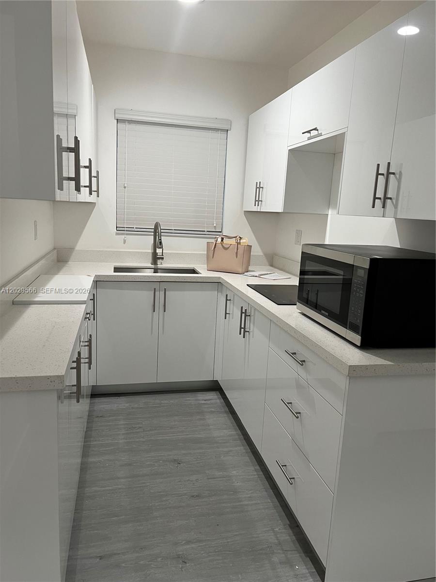 A galley kitchen features white high-gloss cabinets, light countertops, and gray wood-look flooring — 502 & 510 SW 27th Ave, Miami FL 33135, MIAMI, FL