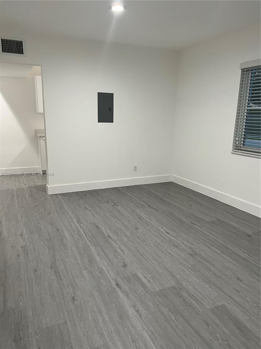 An empty room features gray wood-look flooring, white walls, a window with blinds, and a doorway — 502 & 510 SW 27th Ave, Miami FL 33135, MIAMI, FL