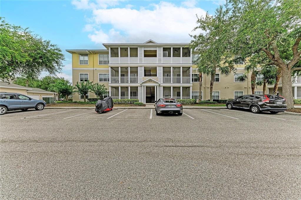 A three-story apartment building with screened balconies sits behind a parking lot with several cars — 4802 51ST STREET W UNIT 416, BRADENTON, FL