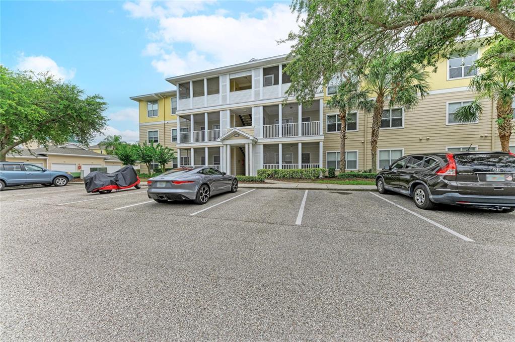 A three-story apartment building with screened balconies sits behind a paved parking lot — 4802 51ST STREET W UNIT 416, BRADENTON, FL