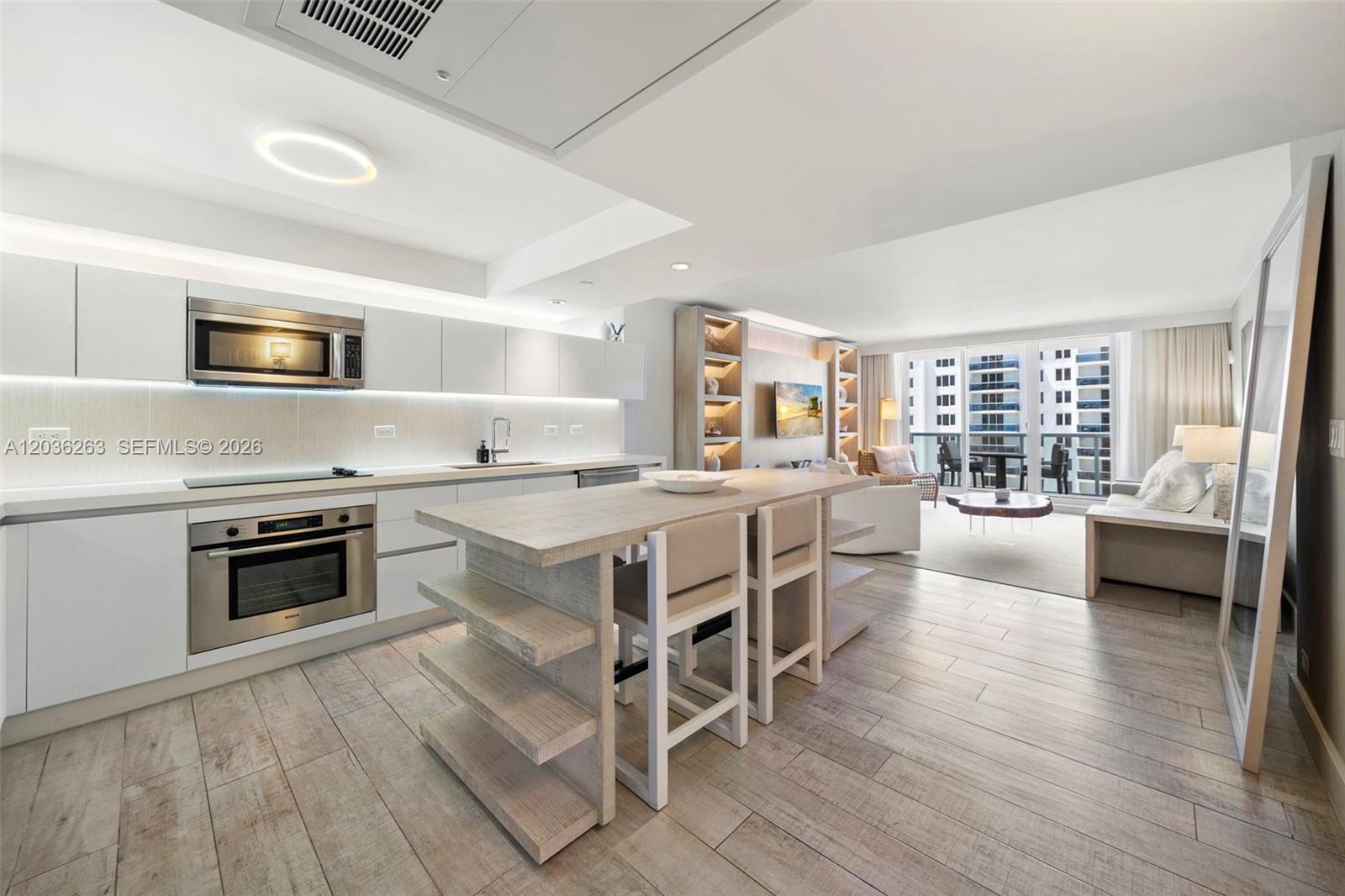 A modern kitchen with a wooden island and white cabinetry opens into a living area — 102 24th St # 1210, Miami Beach FL 33139, MIAMI BEACH, FL