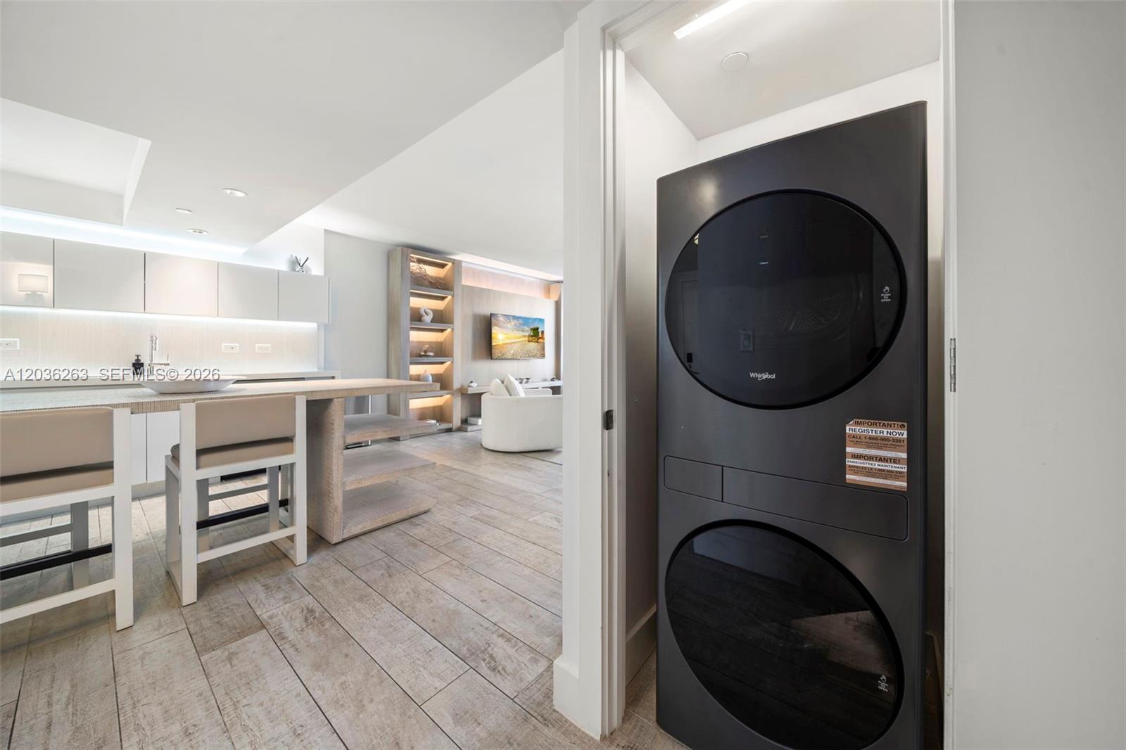 A modern kitchen with a breakfast bar overlooks a living area containing a stacked washer-dryer — 102 24th St # 1210, Miami Beach FL 33139, MIAMI BEACH, FL