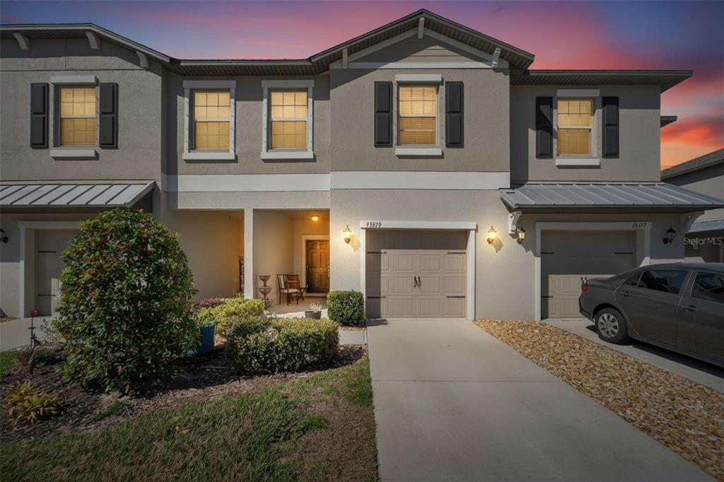 A two-story townhouse exterior features a beige stucco facade, a garage, and a covered entryway — 15519 PRESTWICK ROSE PLACE, SUN CITY CENTER, FL