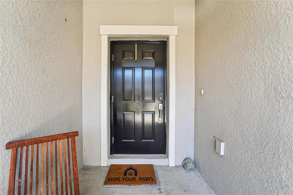 A black front door with a white frame and a pet-themed doormat on a porch — 15519 PRESTWICK ROSE PLACE, SUN CITY CENTER, FL