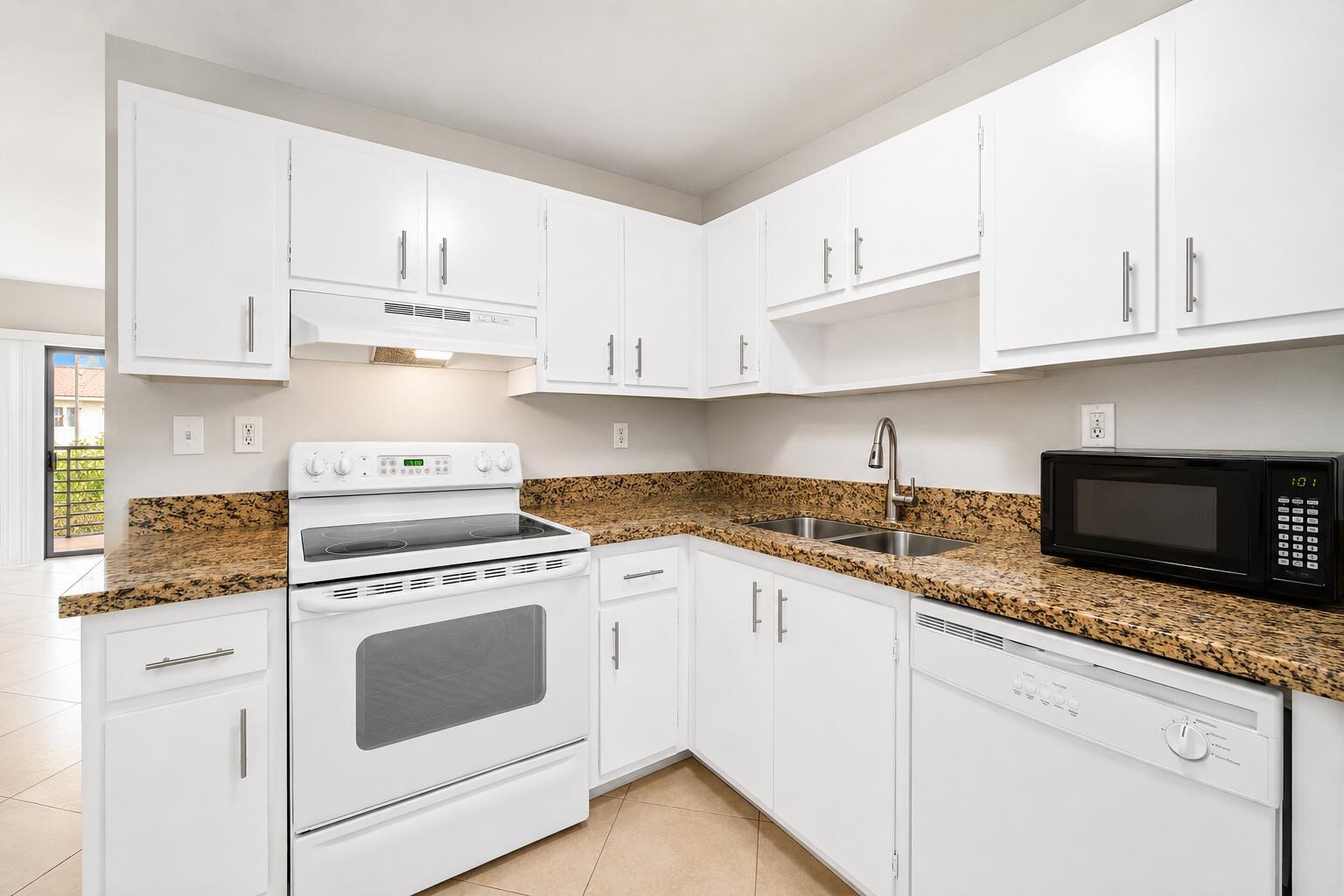 A kitchen features white cabinets, granite countertops, a white stove, and a stainless steel sink — 503 Gardens Drive # 202, Pompano Beach FL 33069, POMPANO BEACH, FL