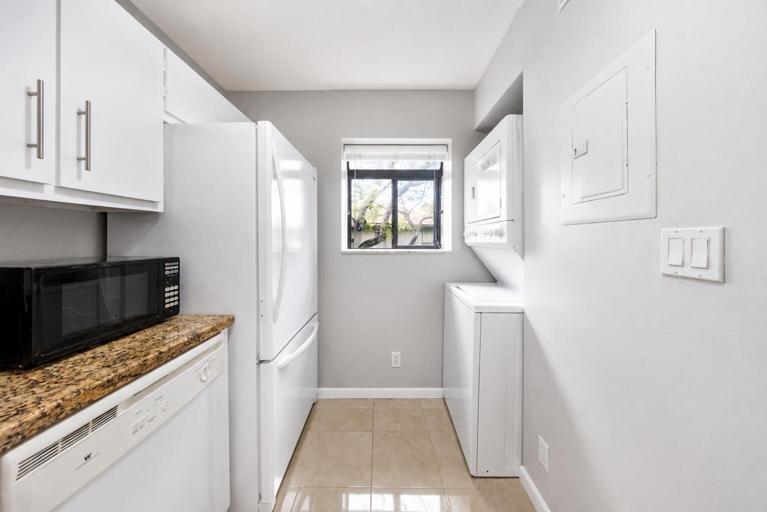 A small kitchen and laundry area features white cabinets, appliances, and a window — 503 Gardens Drive # 202, Pompano Beach FL 33069, POMPANO BEACH, FL