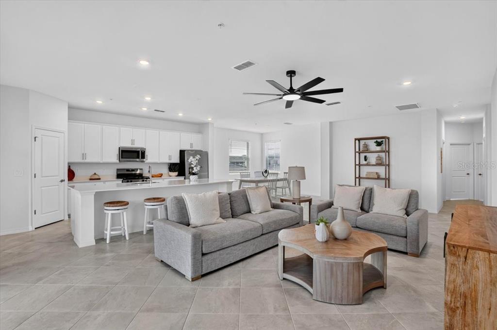 An open-concept living room and kitchen feature white cabinetry, gray sofas, and tile flooring — 19209 CHERRYSTONE WAY UNIT 103, LAKEWOOD RANCH, FL