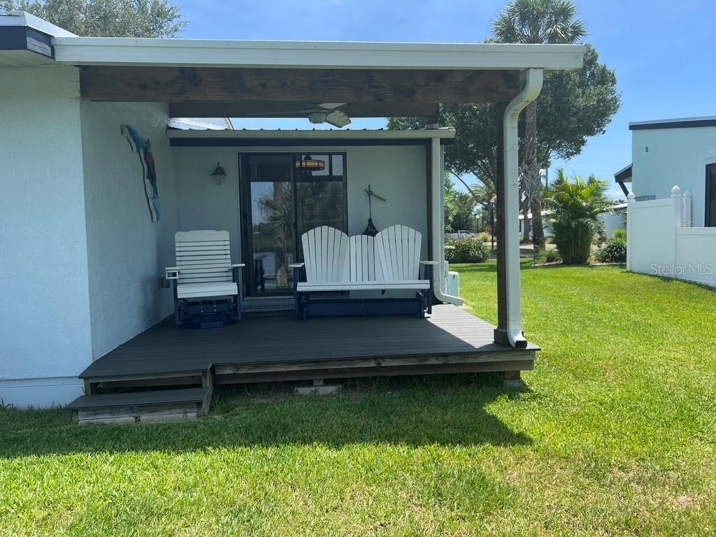 A covered wooden deck with outdoor seating sits attached to the side of a house — 76 HEATHER POINT COURT, NEW SMYRNA BEACH, FL