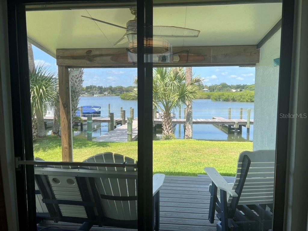 A view from inside through a sliding glass door looking out onto a waterfront deck — 76 HEATHER POINT COURT, NEW SMYRNA BEACH, FL