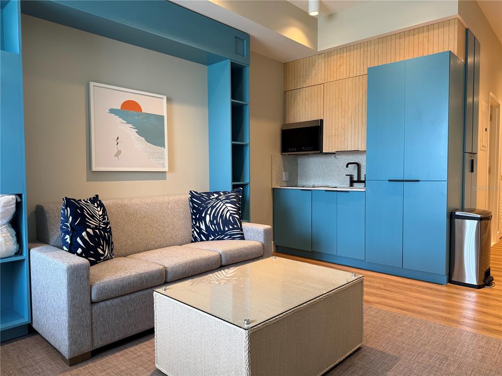A studio living area features a sofa, glass coffee table, and a blue kitchenette — 8050 VACATION AVENUE UNIT 302, KISSIMMEE, FL