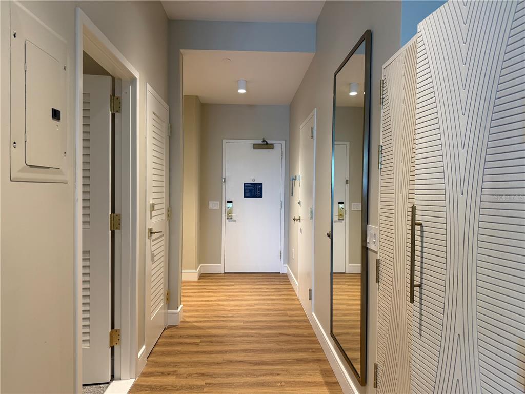 A hallway with wood-look flooring, white doors, a tall mirror, and a textured cabinet — 8050 VACATION AVENUE UNIT 302, KISSIMMEE, FL