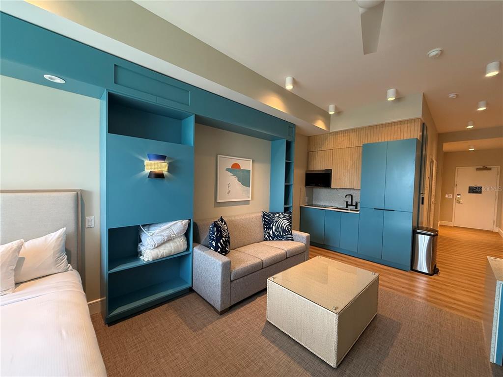 A studio apartment features a sofa, a kitchenette with blue cabinets, and a bed — 8050 VACATION AVENUE UNIT 302, KISSIMMEE, FL