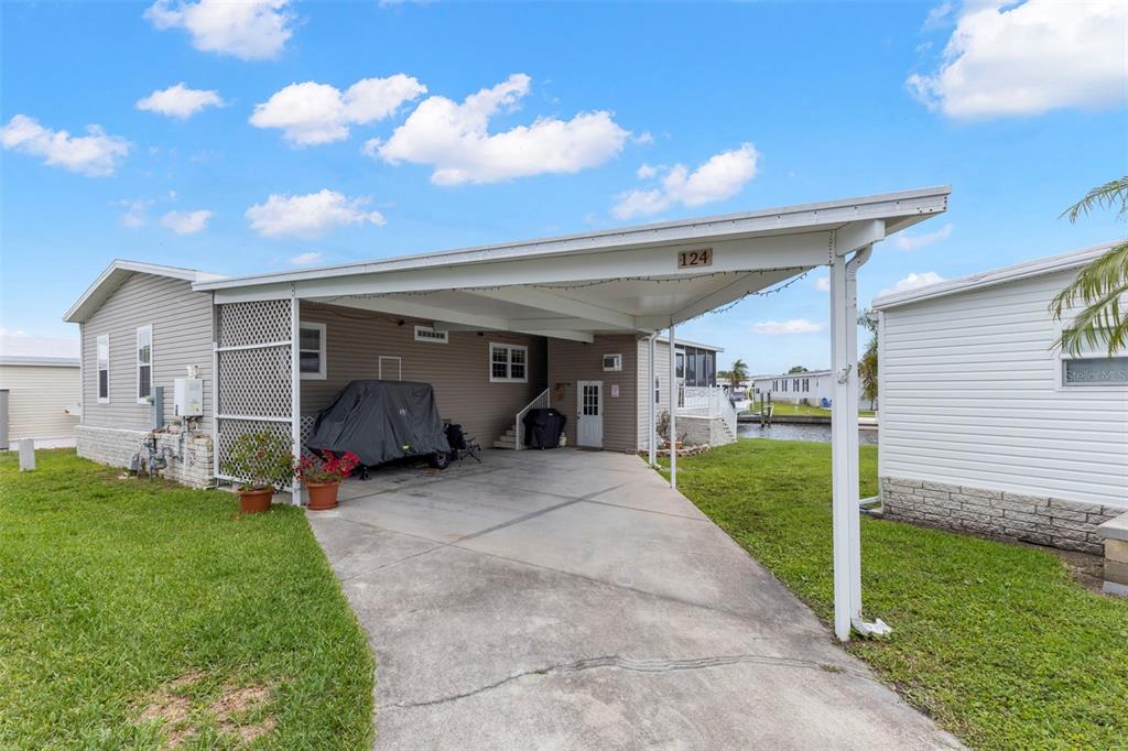 A manufactured home with a concrete driveway, a large carport, and a view of water — 124 AMERICANA COURT NE UNIT 214, ST PETERSBURG, FL