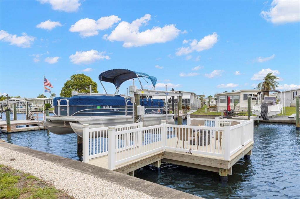 A pontoon boat sits on a lift next to a white deck on a canal — 124 AMERICANA COURT NE UNIT 214, ST PETERSBURG, FL