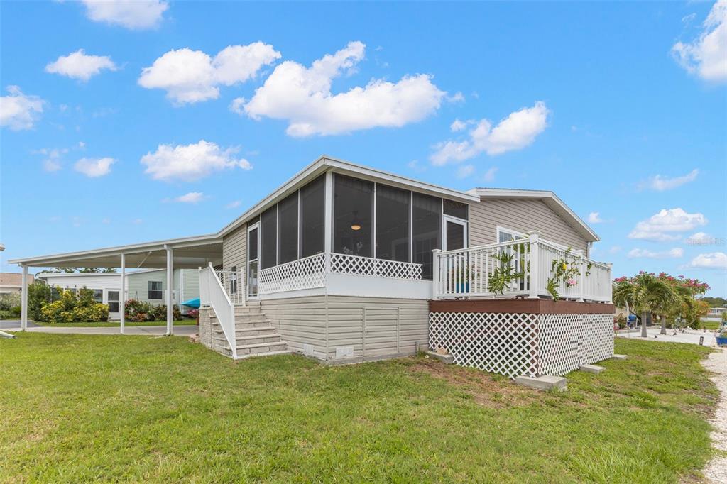 A mobile home with a screened-in porch, an attached carport, and a raised wooden deck — 124 AMERICANA COURT NE UNIT 214, ST PETERSBURG, FL