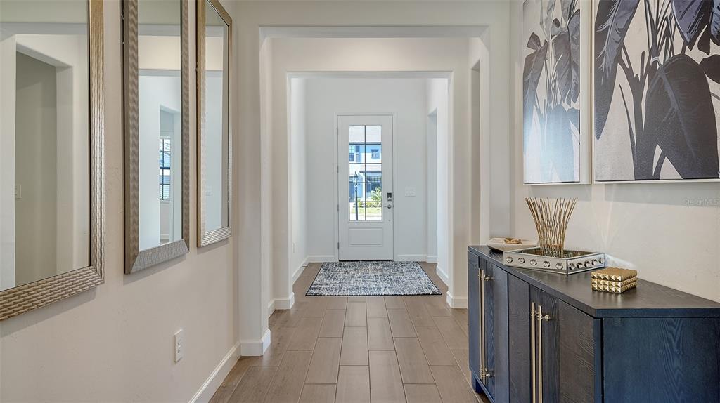 A bright entryway features wood-look tile floors, a dark console table, and a glass-paneled door — 4909 OYSTER PEARL STREET, LAKEWOOD RANCH, FL