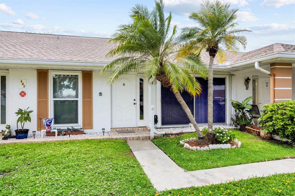 The exterior of a single-story residential building features a white door, palm trees, and landscaping — 127 LAKES END DRIVE UNIT C, FORT PIERCE, FL