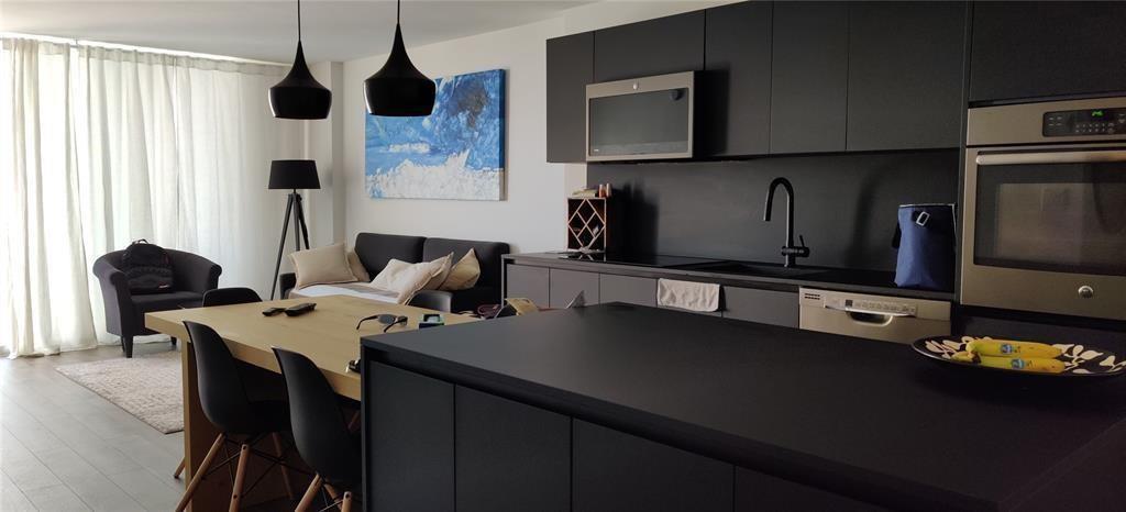 A modern open-concept kitchen and living area featuring dark cabinetry and a wooden dining table — 345 Ocean Drive # 512, Miami Beach FL 33139, MIAMI BEACH, FL