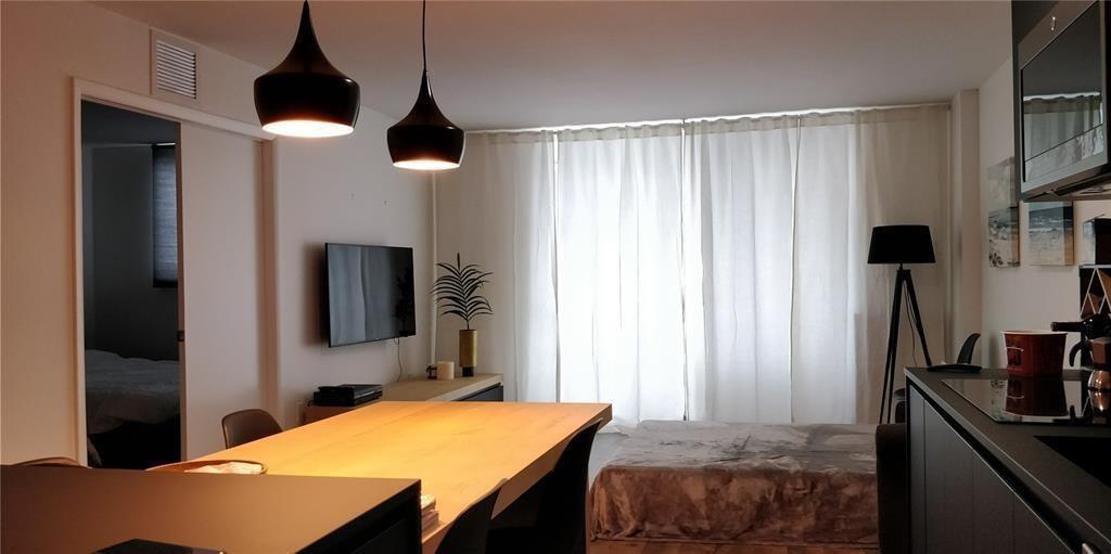 A modern living area features a dining table, pendant lights, a television, and floor-to-ceiling curtains — 345 Ocean Drive # 512, Miami Beach FL 33139, MIAMI BEACH, FL