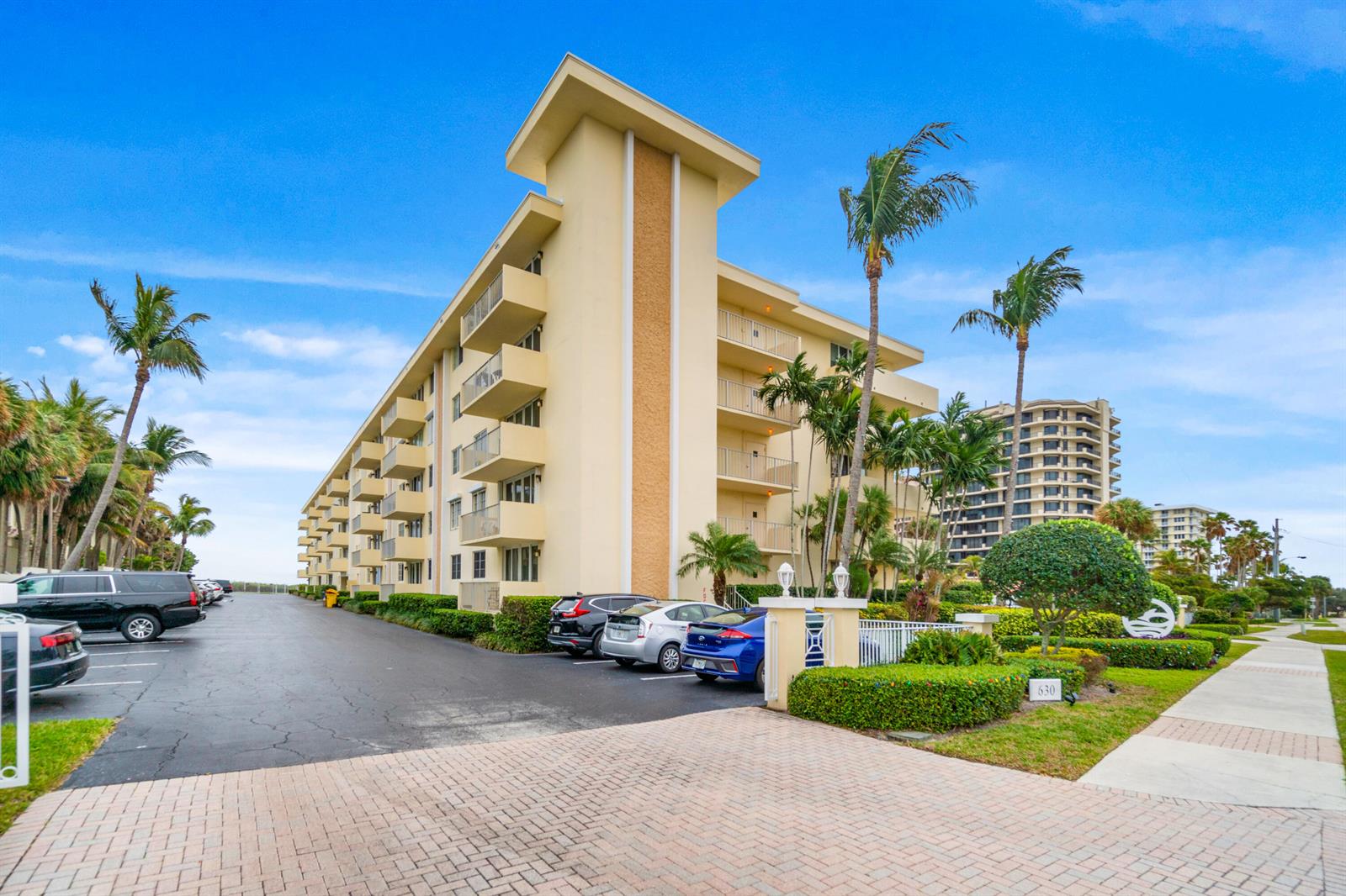 A multi-story yellow apartment building with balconies stands next to a parking lot — 630 Ocean Drive # 410, Juno Beach FL 33408, JUNO BEACH, FL