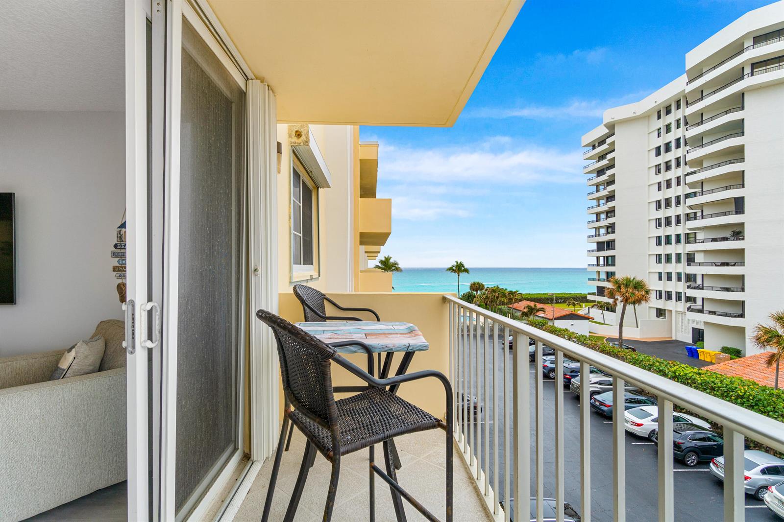 A balcony with two chairs and a table overlooks a parking lot and the ocean — 630 Ocean Drive # 410, Juno Beach FL 33408, JUNO BEACH, FL