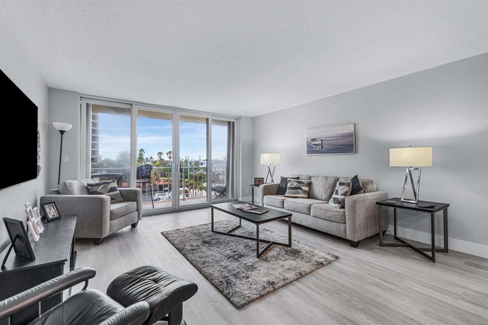 A living room features gray furniture, a dark coffee table, and sliding doors to a balcony — 630 Ocean Drive # 410, Juno Beach FL 33408, JUNO BEACH, FL