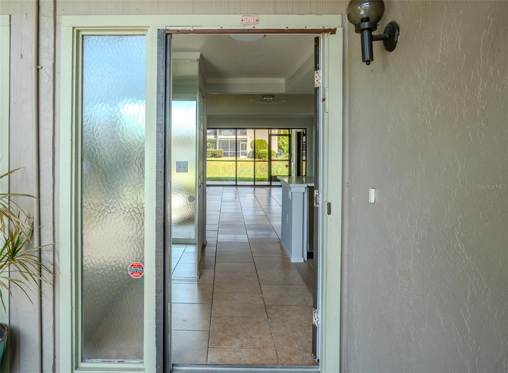 An open front door reveals a tiled entryway leading to a living area with large windows — 5797 SUMMER SIDE LANE UNIT 7A, SARASOTA, FL