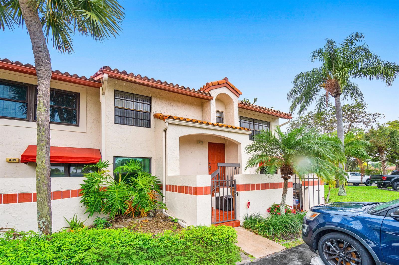 A two-story stucco townhouse features a red tile roof, red awnings, and a gated entrance — 312 Liberty Court, Deerfield Beach FL 33442, DEERFIELD BEACH, FL