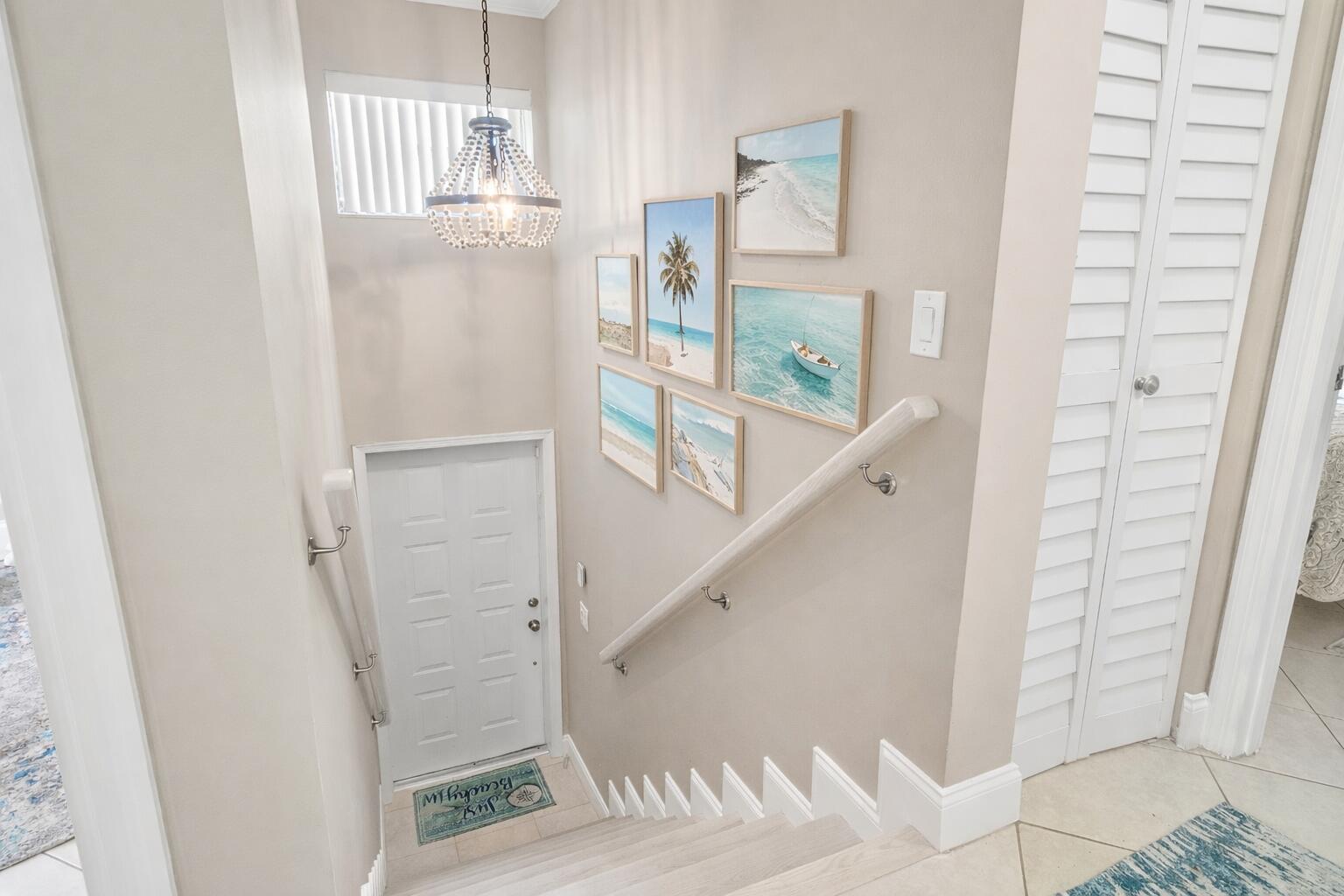 A staircase with a gallery wall of beach-themed art leads down to a white door — 312 Liberty Court, Deerfield Beach FL 33442, DEERFIELD BEACH, FL