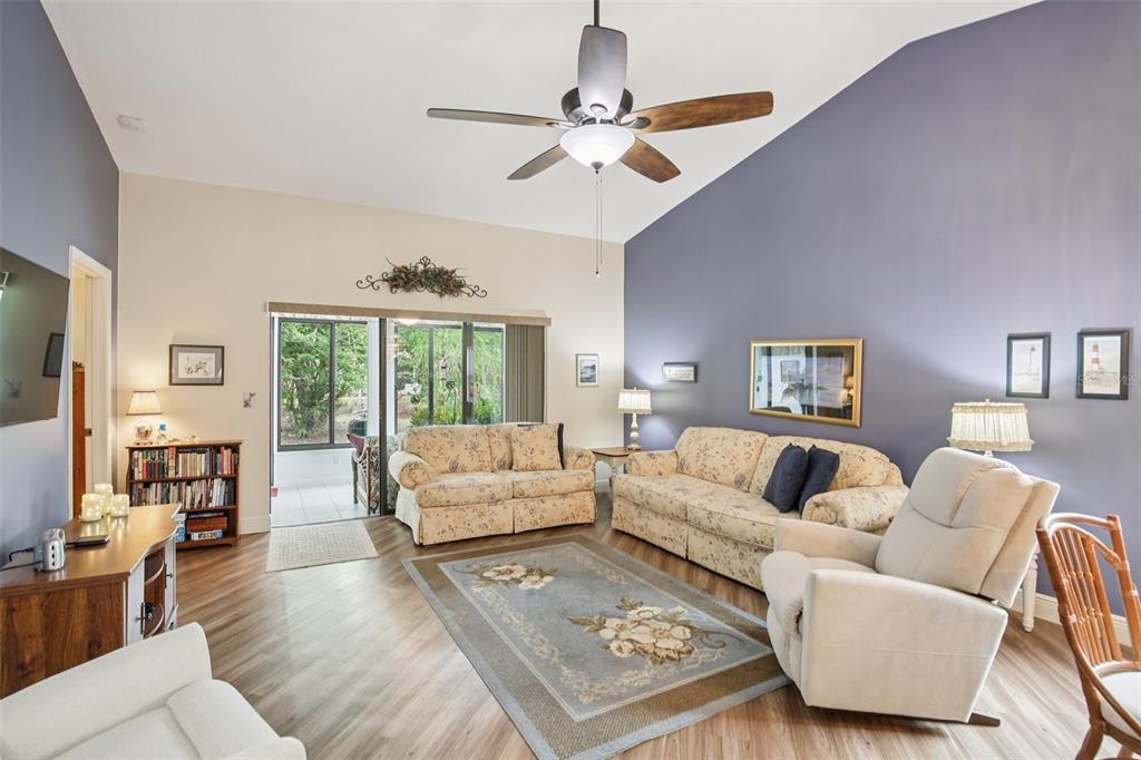 A living room with a vaulted ceiling, floral sofas, a ceiling fan, and wood flooring — 11622 COCOWOOD DRIVE, NEW PORT RICHEY, FL